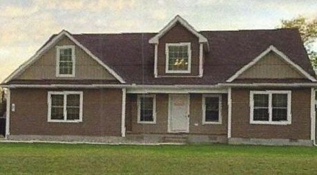 A large brown house with a roof and a lot of windows is sitting on top of a lush green field.