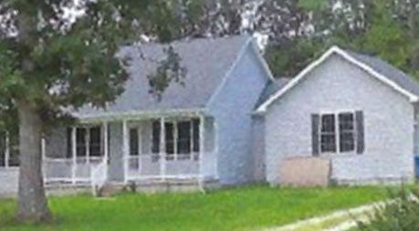 A small white house with a porch and a tree in front of it.