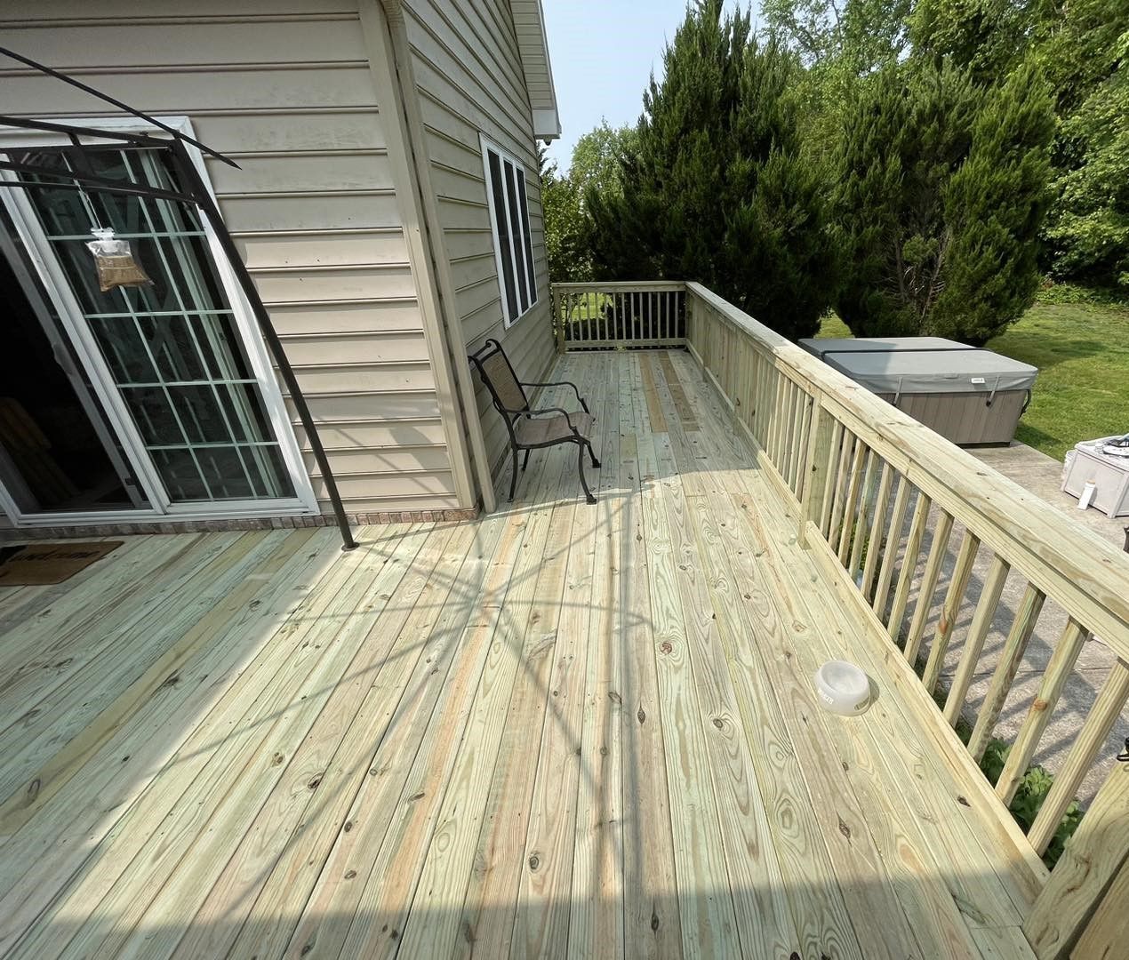 A large wooden deck with a chair and a hot tub in the backyard of a house