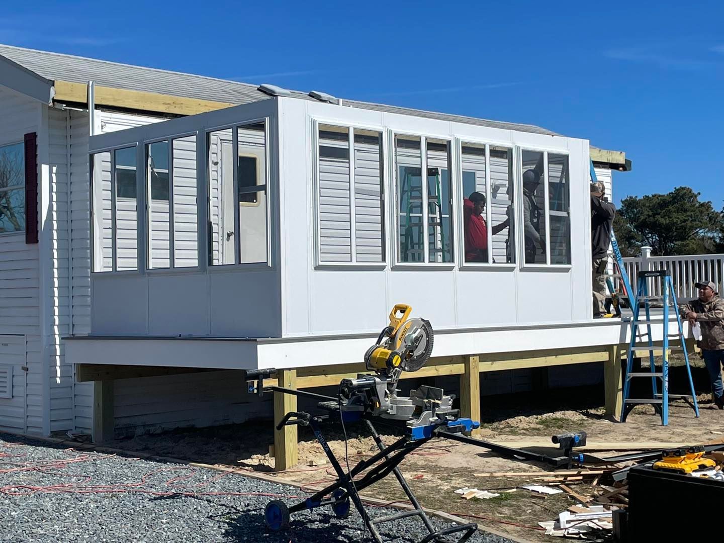 A man is using a circular saw to build a sunroom on the side of a house.