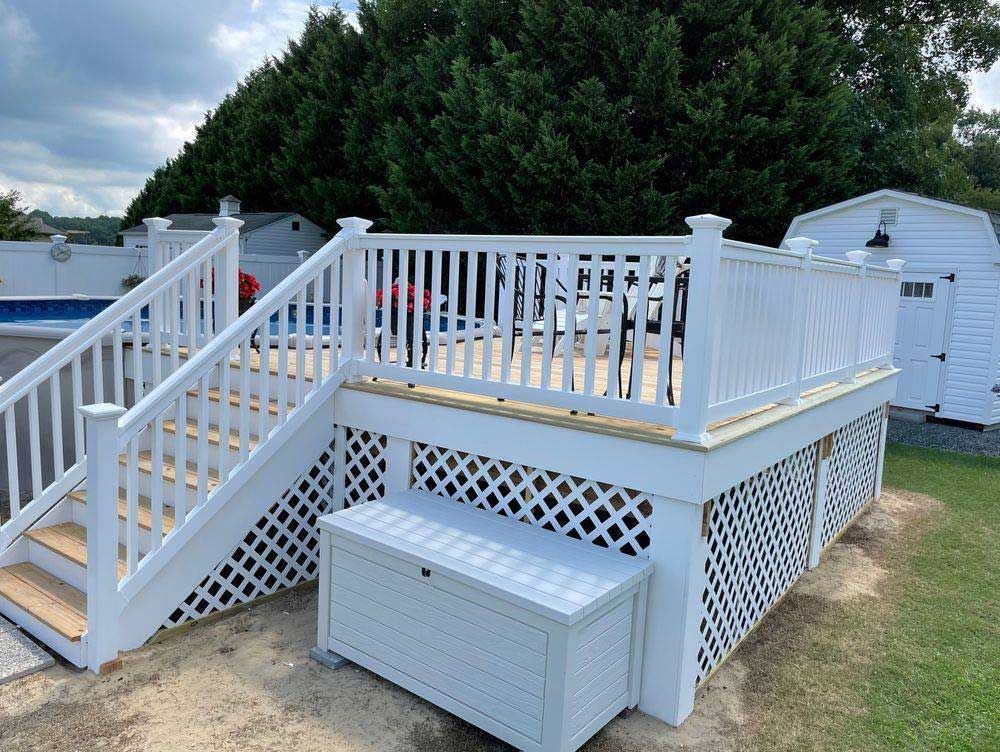 A white deck with stairs and a bench next to a pool.