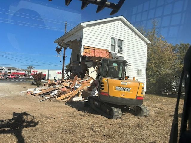 A yellow excavator is demolishing a white house.