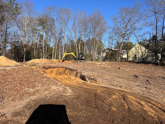 A yellow excavator is digging a hole in a dirt field.