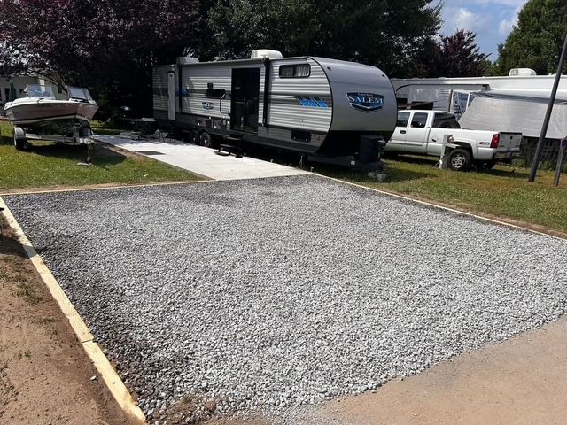 A trailer is parked in a gravel lot next to a boat.