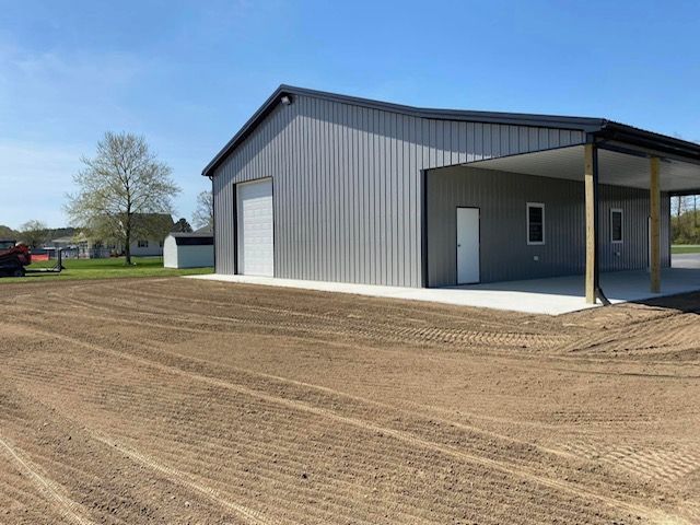 A large metal building with a porch is sitting on top of a dirt field.