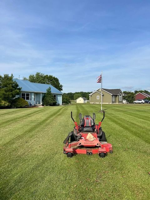A red lawn mower is sitting in a lush green field in front of a house.