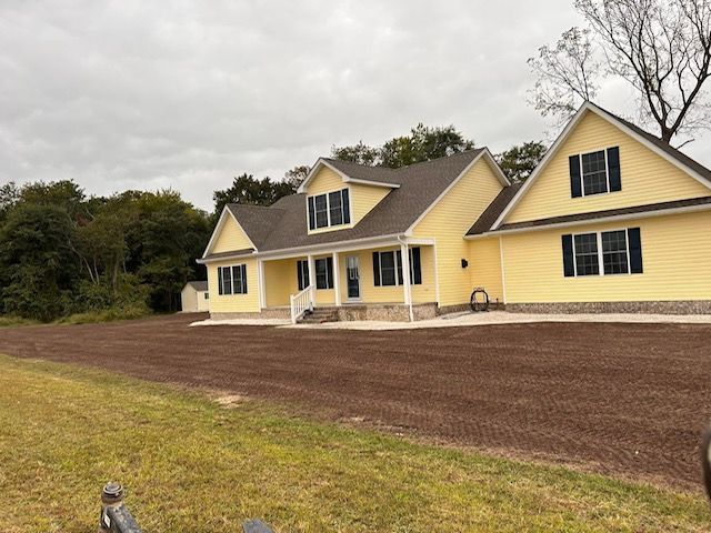 A yellow house with a brown roof is sitting in the middle of a grassy field.