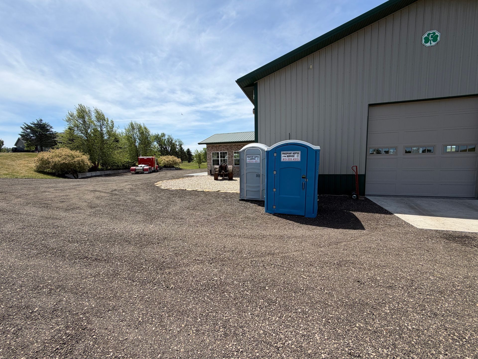 Portable toilets beside a gray metal building on a gravel lot under a blue sky.