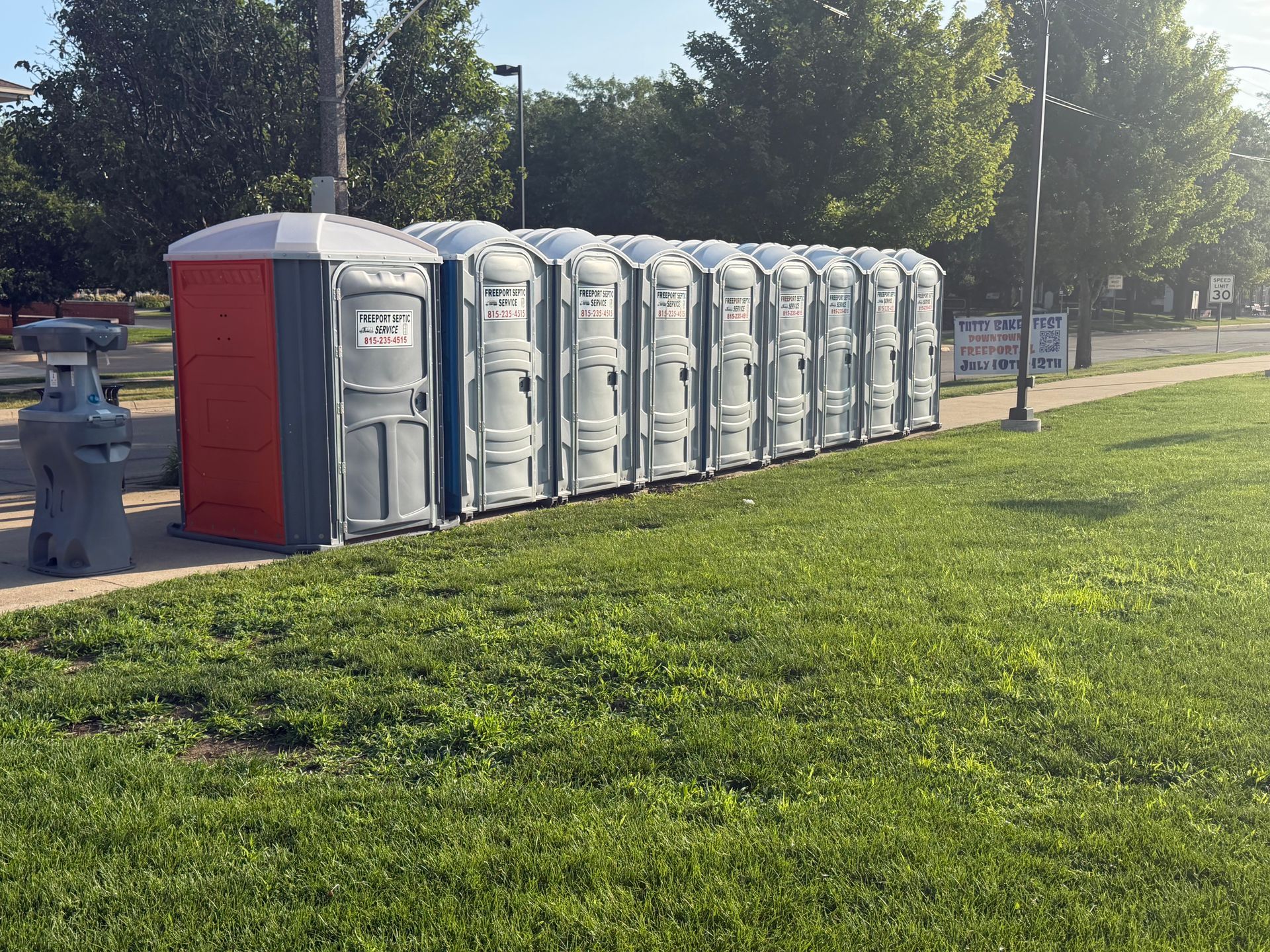 Row of portable toilets beside a grassy park path on a sunny day