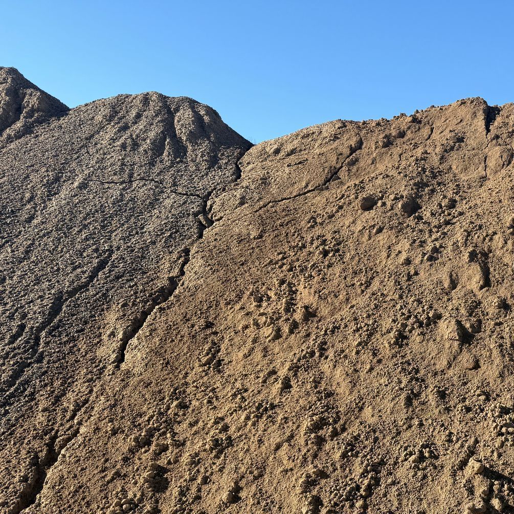 A pile of dirt in a barn with a bulldozer in the background.