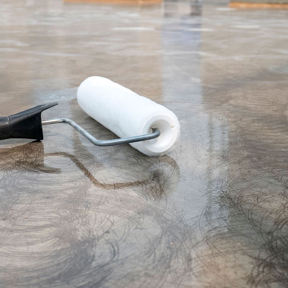 A paint roller is sitting on a wet concrete floor.