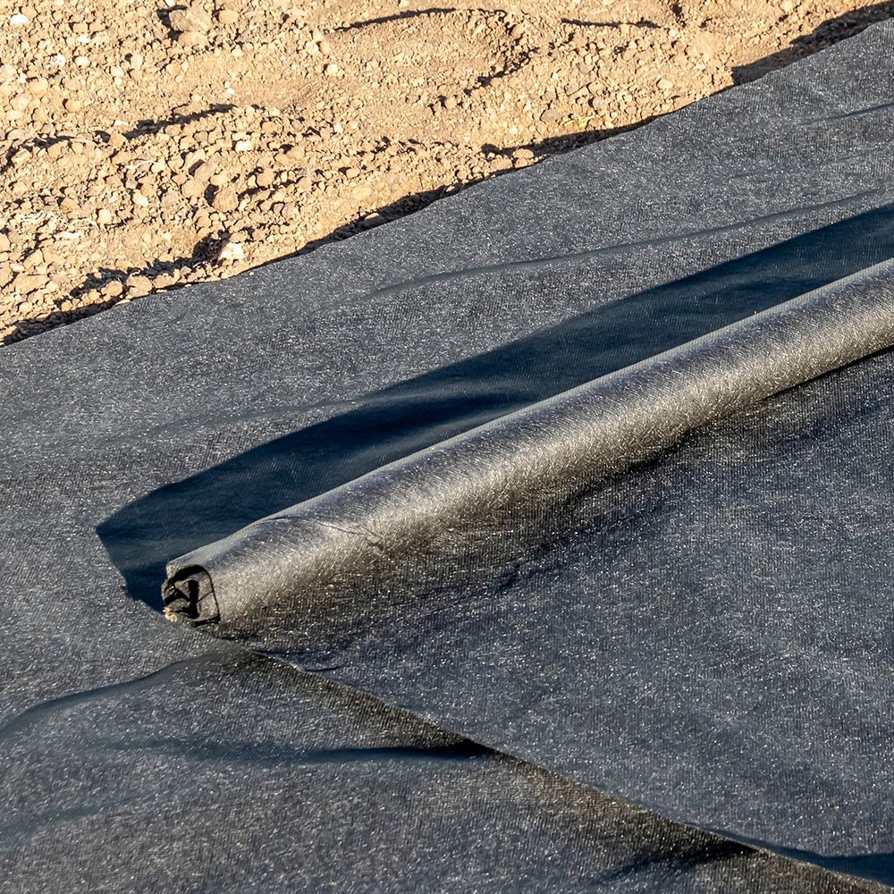 A roll of black fabric is laying on top of a pile of dirt.