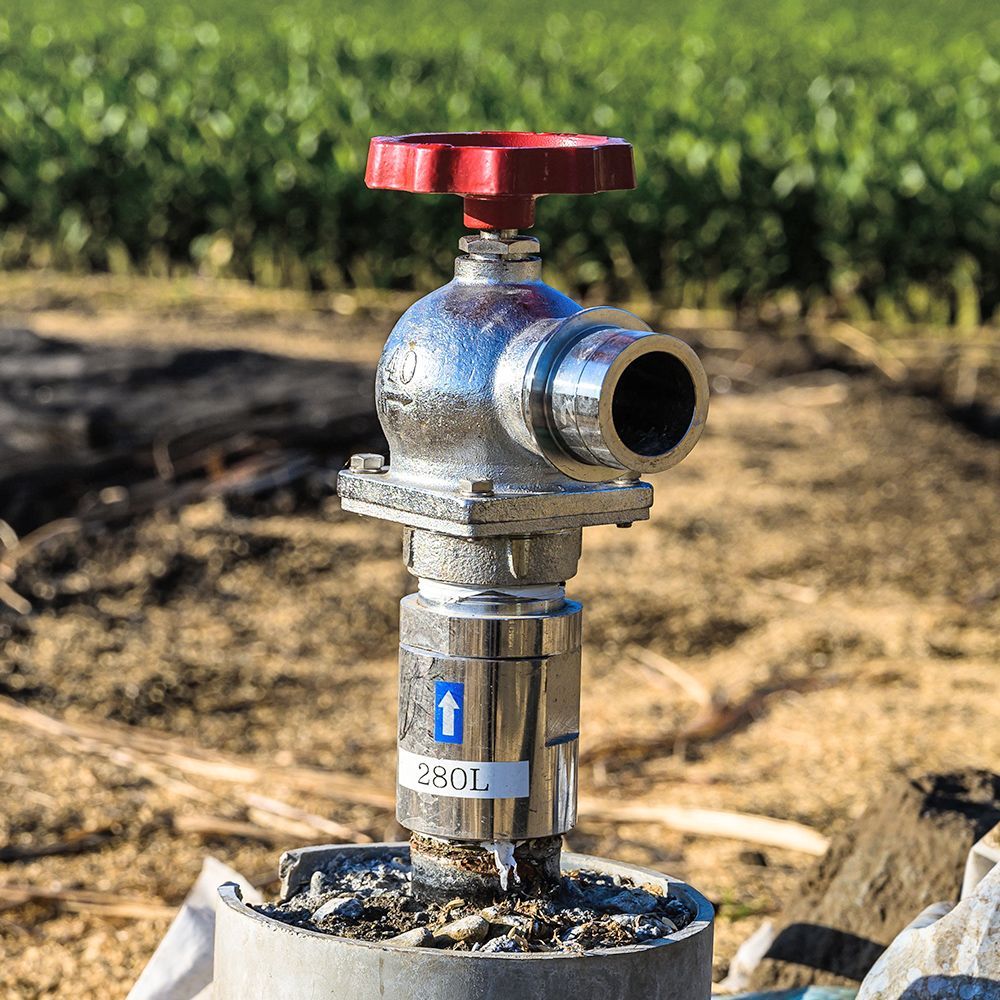 A close up of a valve in a field with a red handle.