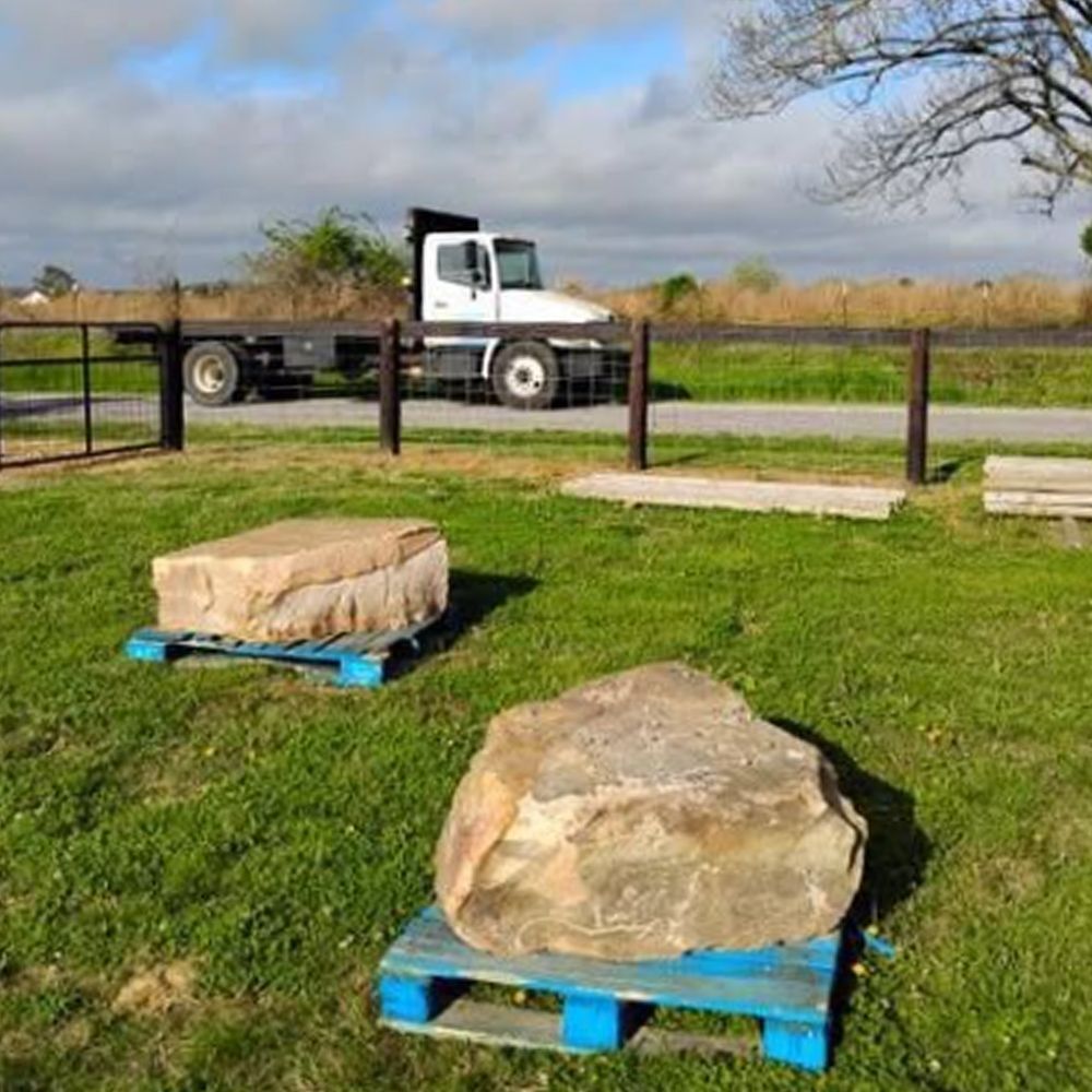 A large rock is sitting on a pallet in a grassy field next to a truck.