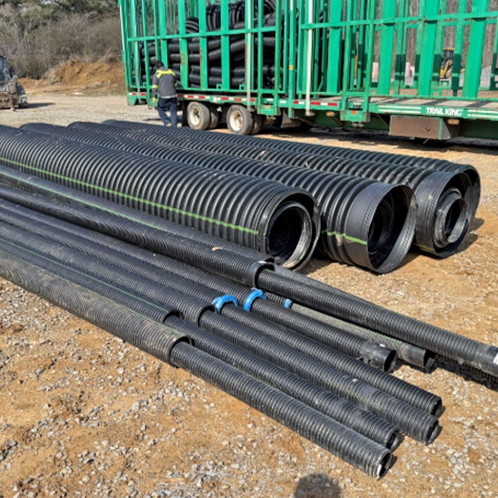 A bunch of black pipes are stacked on top of each other in front of a green truck.