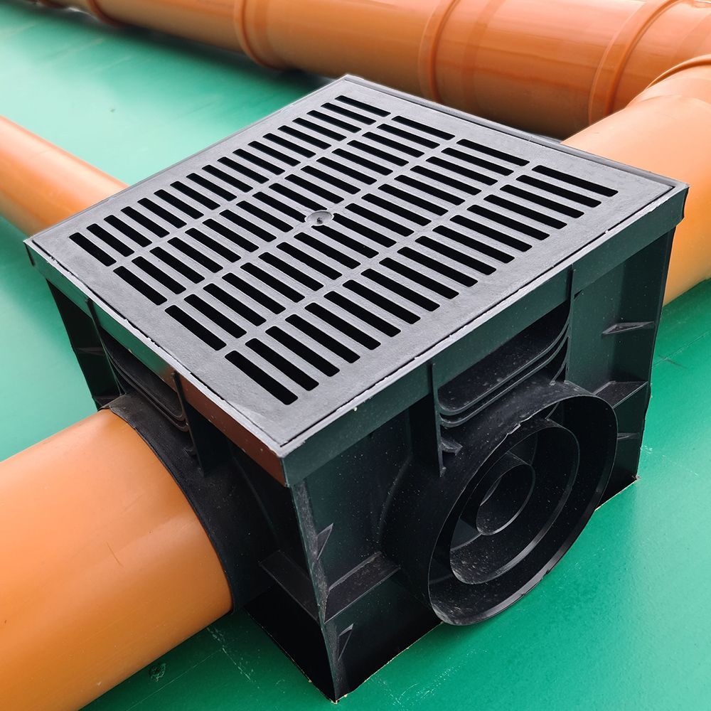 A black drain box is sitting on top of a green table next to orange pipes.