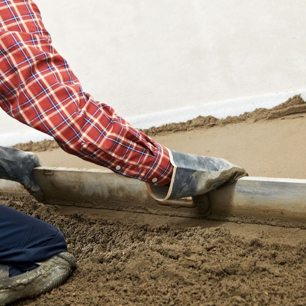 A man is using a screed to level a concrete floor.