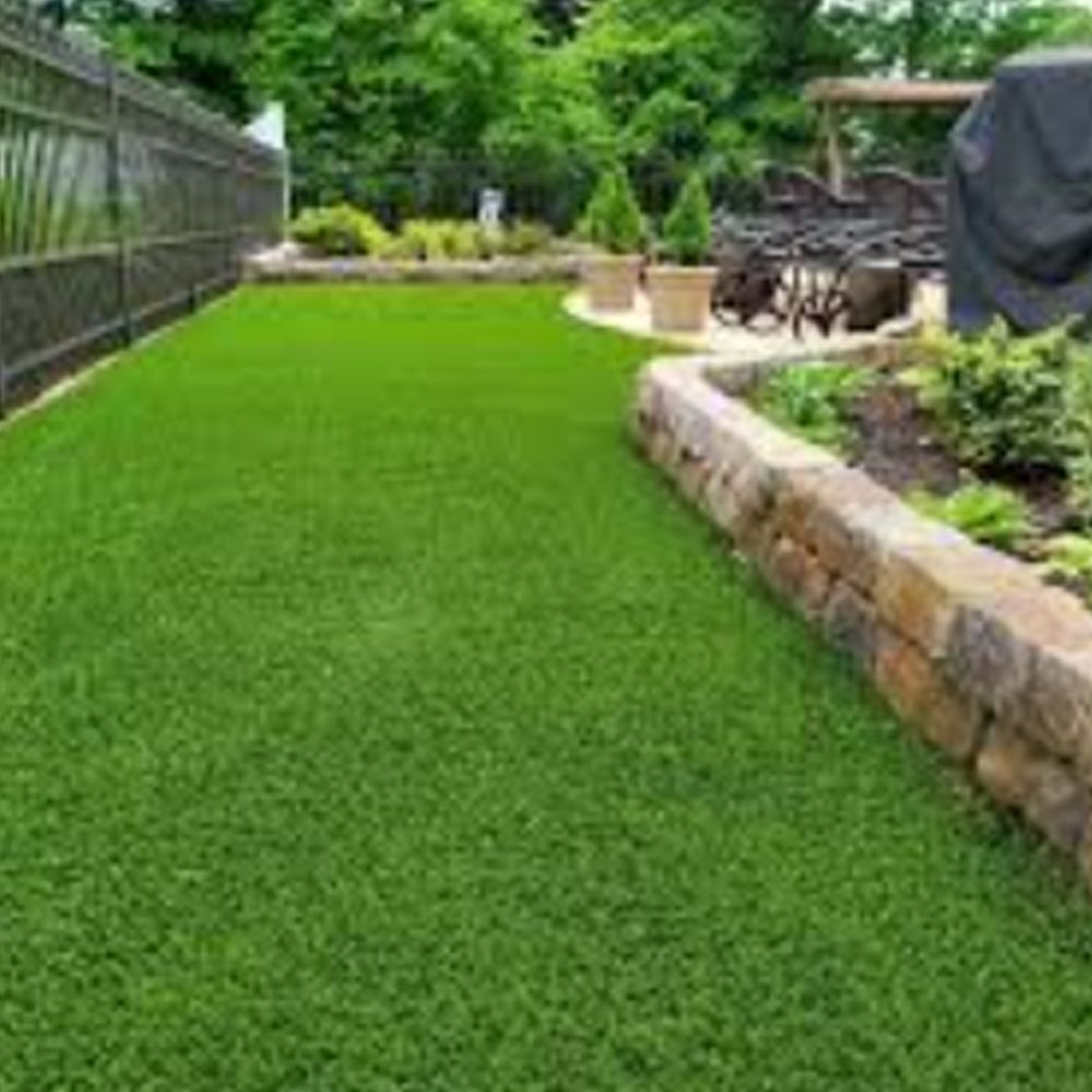 A backyard filled with lots of green grass and a stone wall.