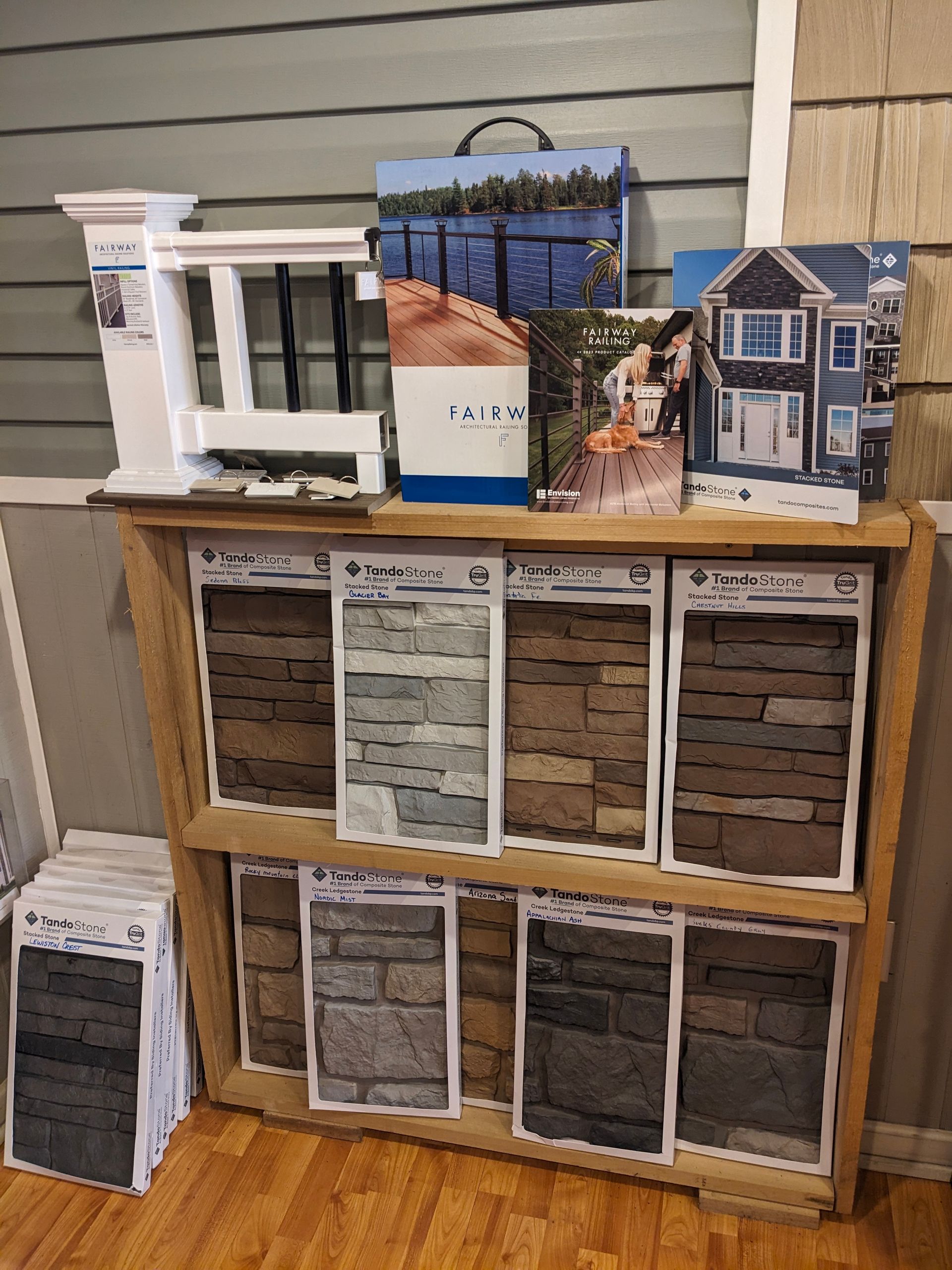 Display of stone siding samples with house and landscape photos above. Wooden shelf on a wood floor.