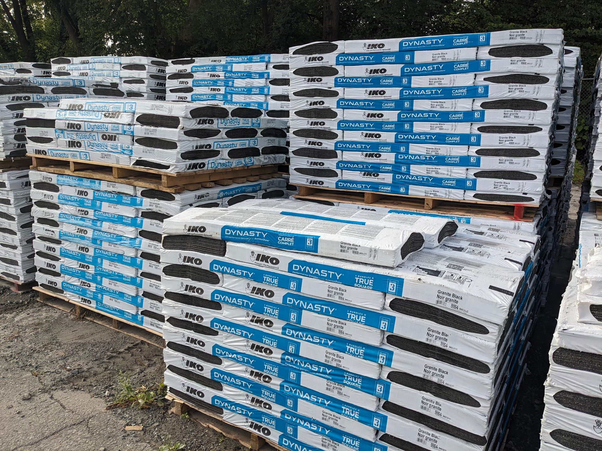 Pallets of asphalt shingles wrapped in blue and white packaging outdoors.