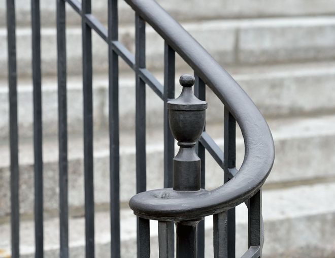 Black metal handrail with decorative finial against a background of gray stairs.