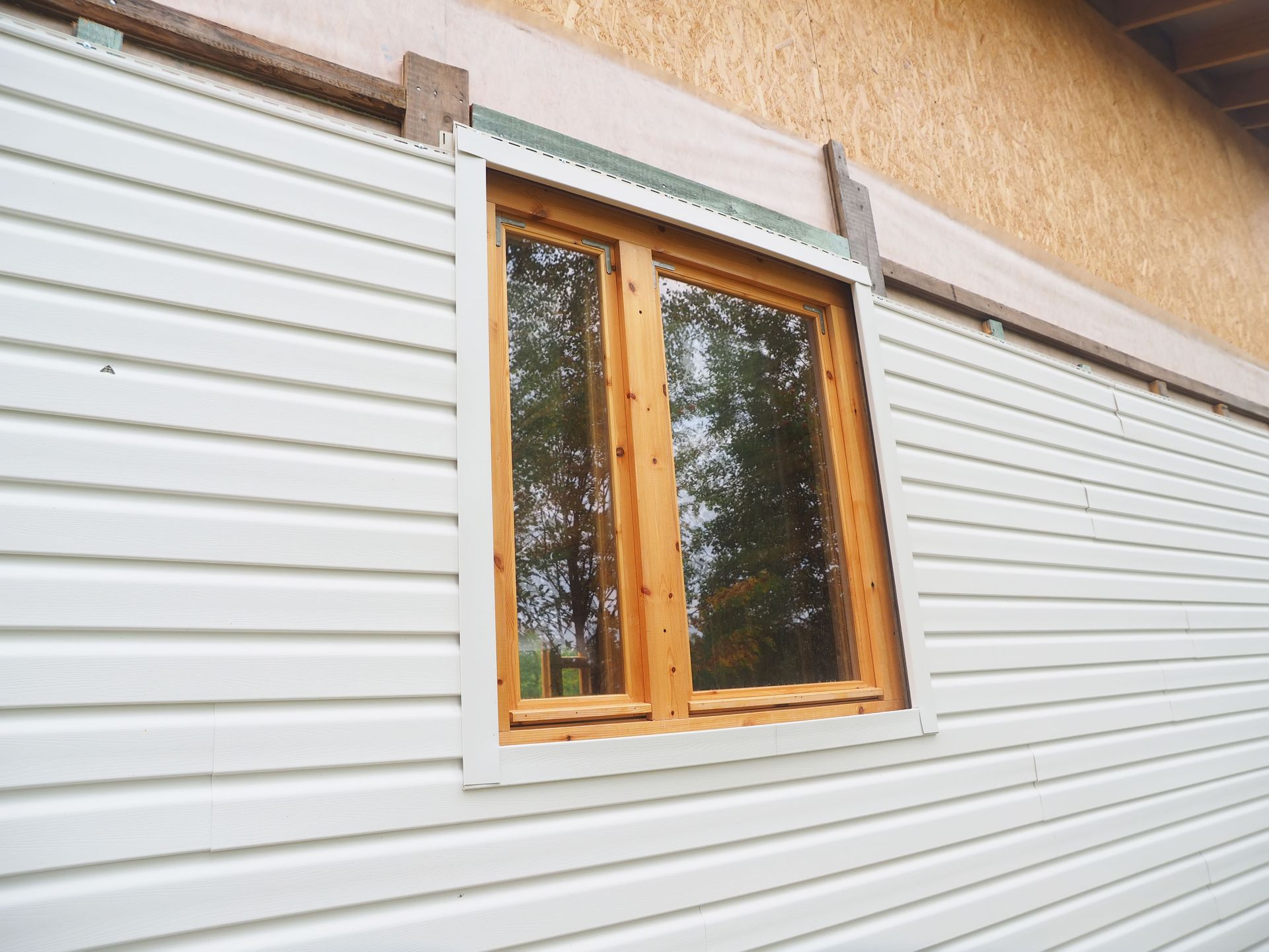 Exterior wall with white siding and a wooden-framed window.