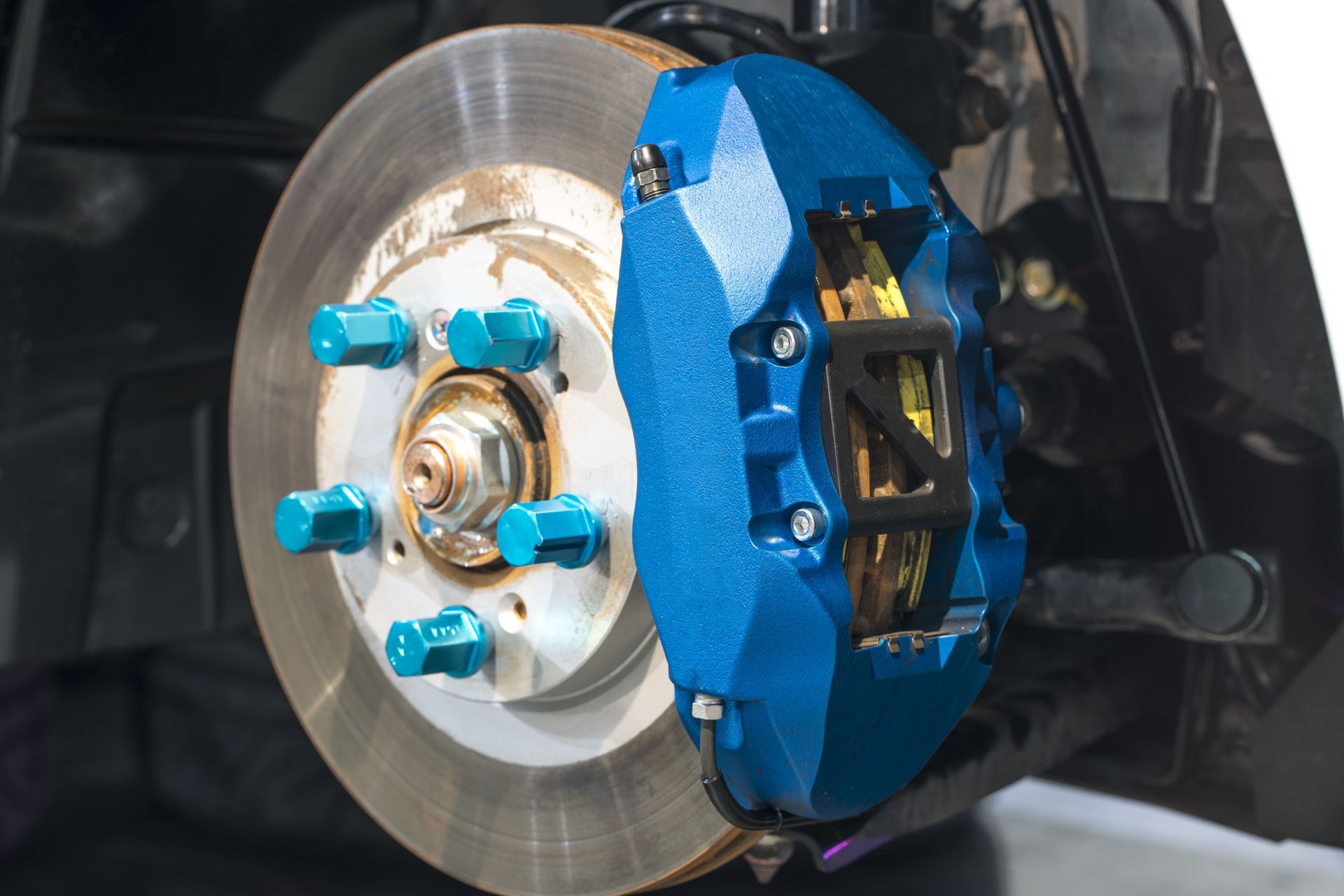 Blue brake caliper on a car, with a silver brake rotor and blue lug nuts.
