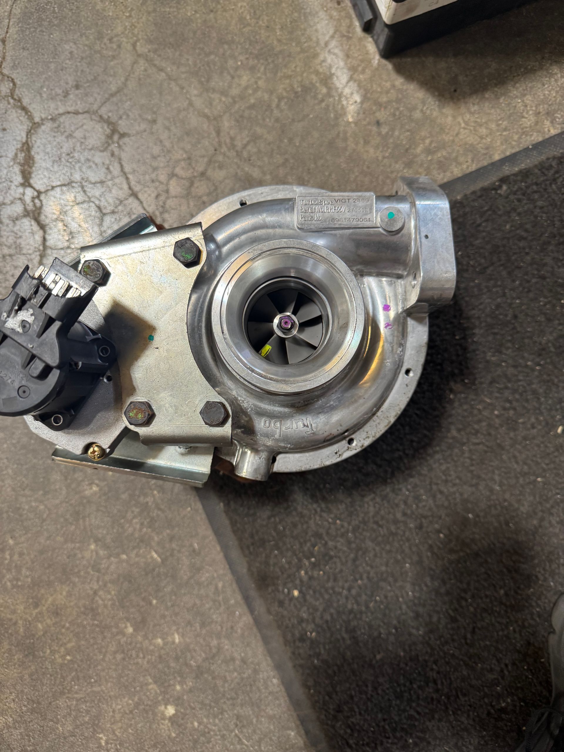Silver turbocharger assembly lying on a concrete floor, with visible turbine blades and black actuator.