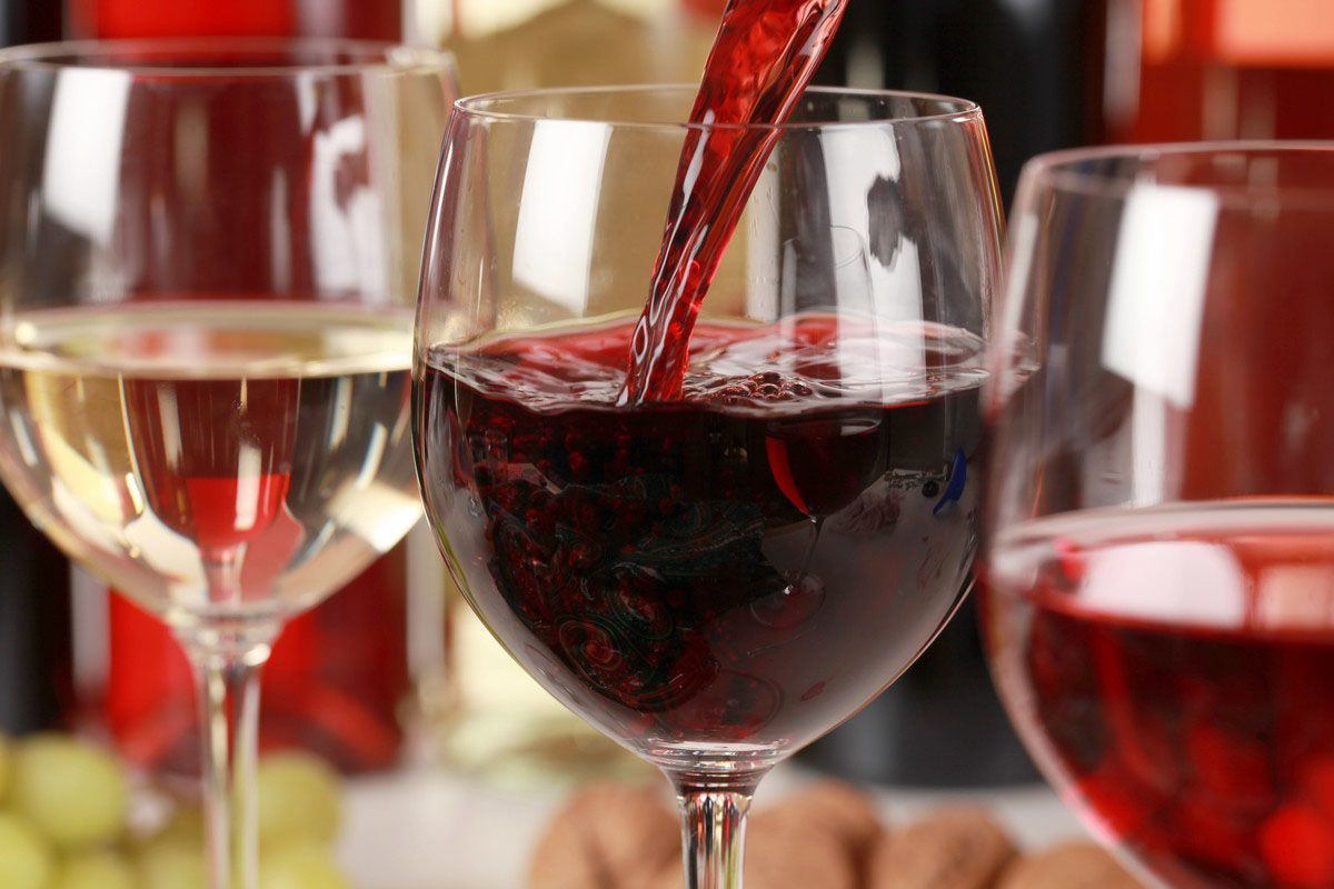 A glass of red wine is being poured into a glass of white wine.