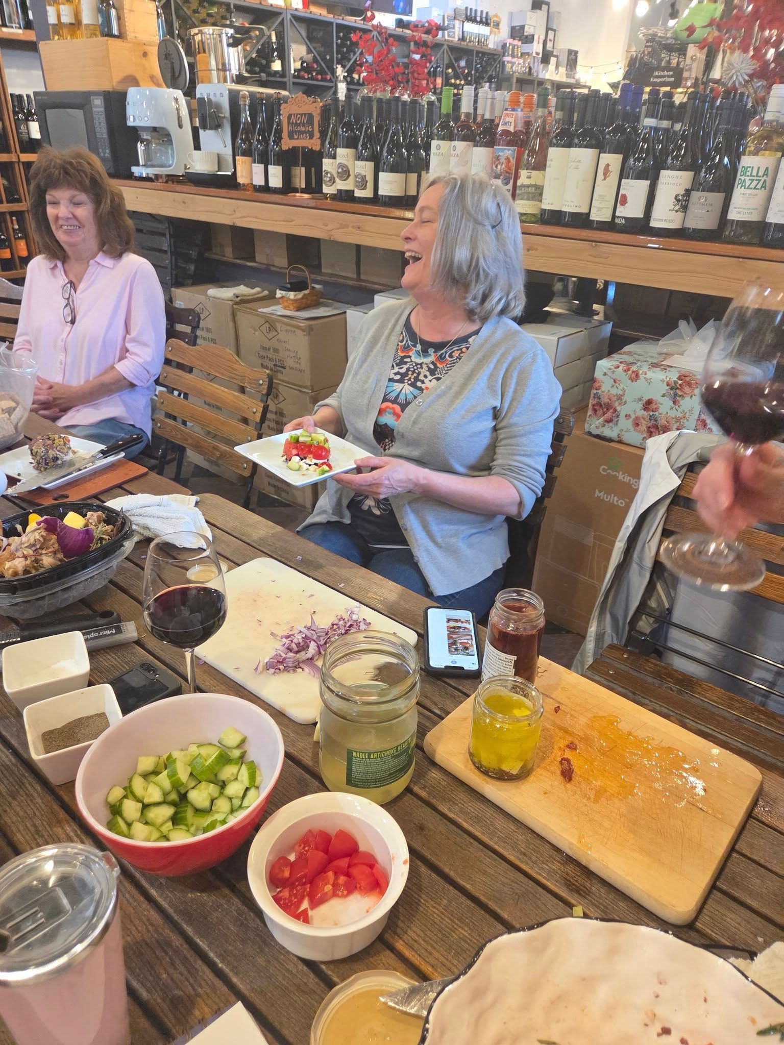 Two women are sitting at a table eating food and drinking wine.