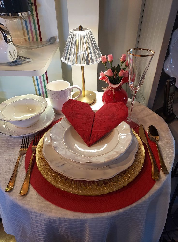 A table with plates , bowls , utensils , and a heart shaped napkin on it.