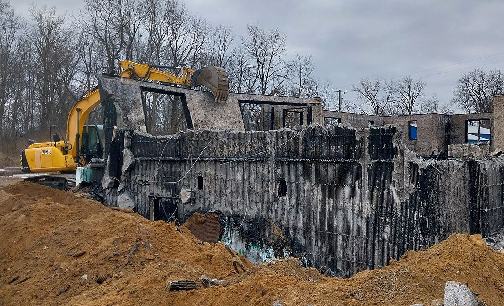 A yellow excavator is destroying a building on a construction site.
