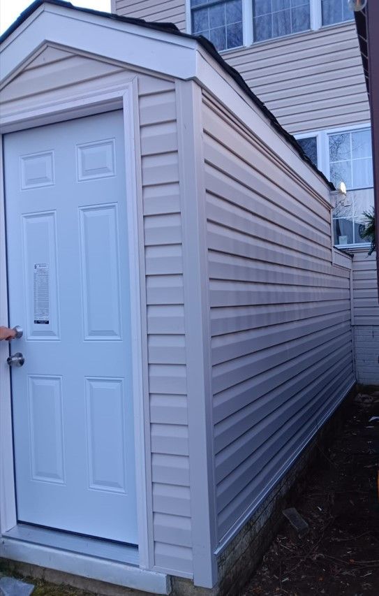 A white shed with a white door is next to a house.