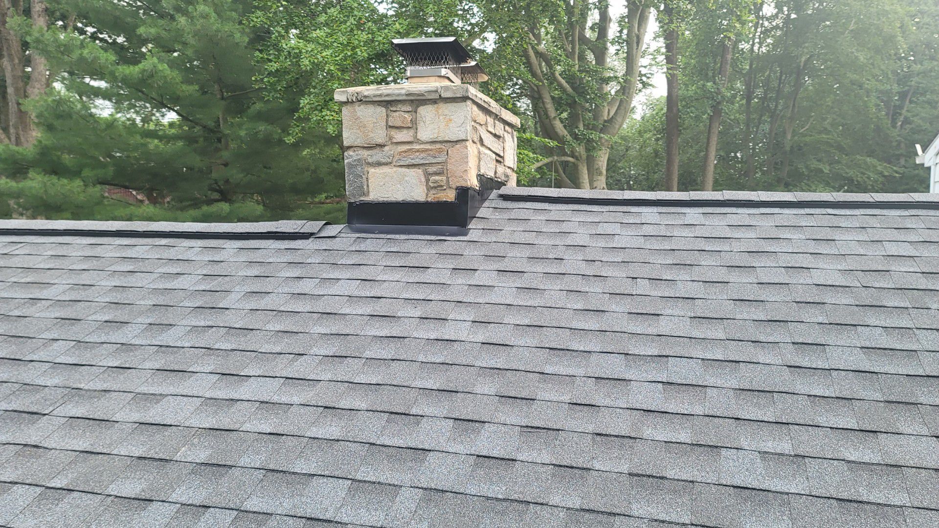 A chimney on top of a roof with trees in the background.
