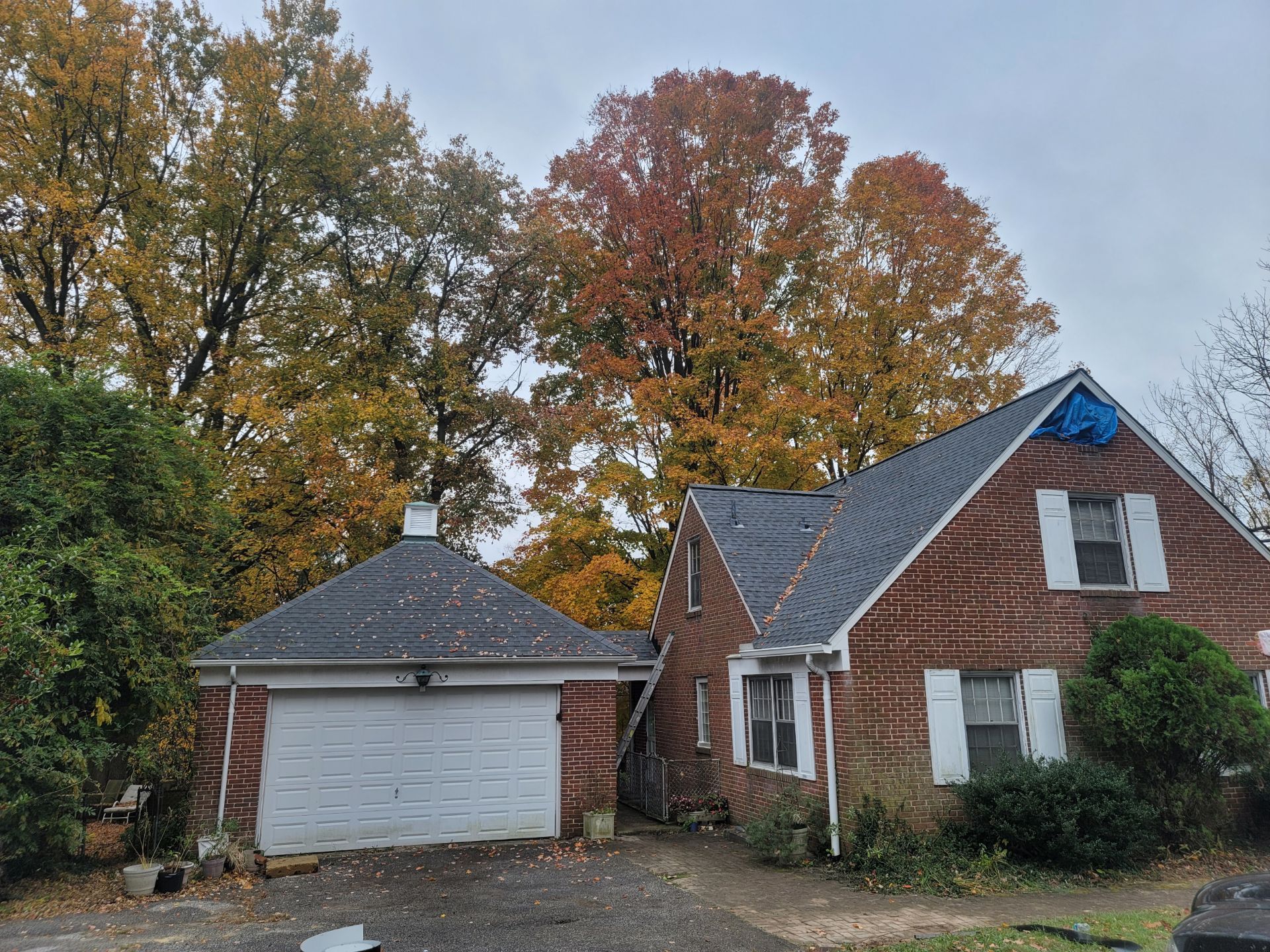 A brick house with a garage and a blue tarp on the roof.