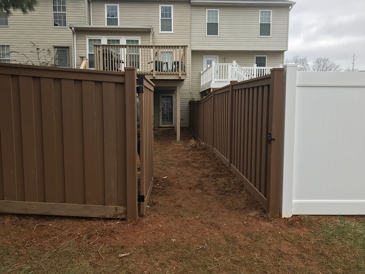 A brown fence with a white gate leading to a house