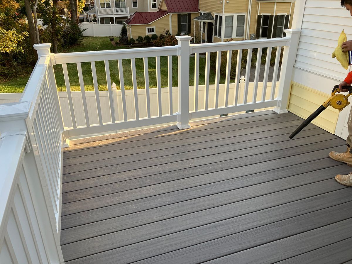 A man is using a blower on a deck with a white railing