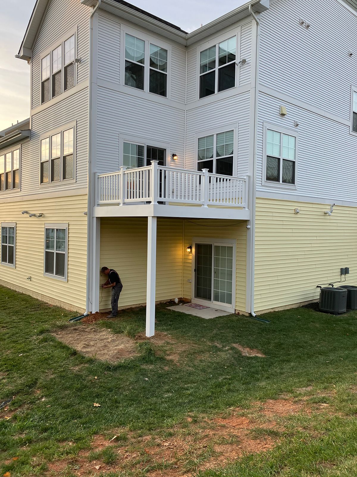 A man is standing in front of a large house with a deck.