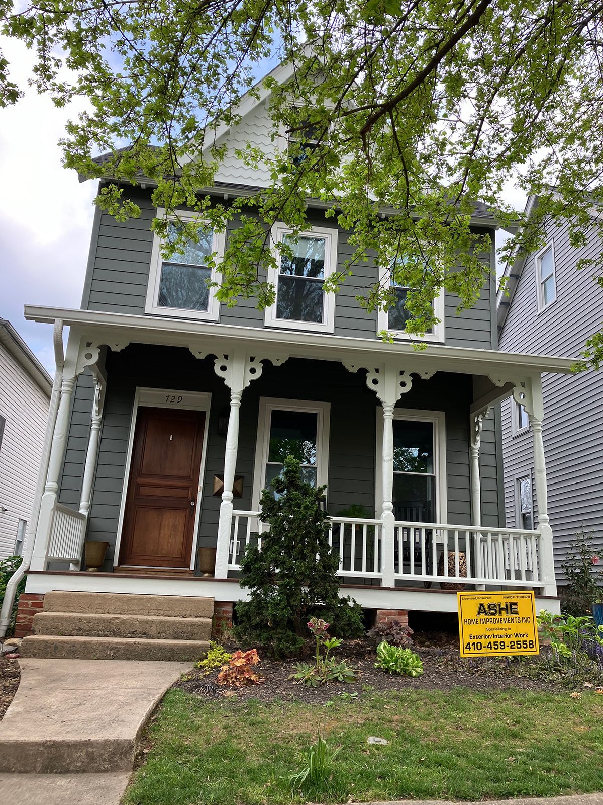 A gray house with a porch and a yellow sign in front of it.