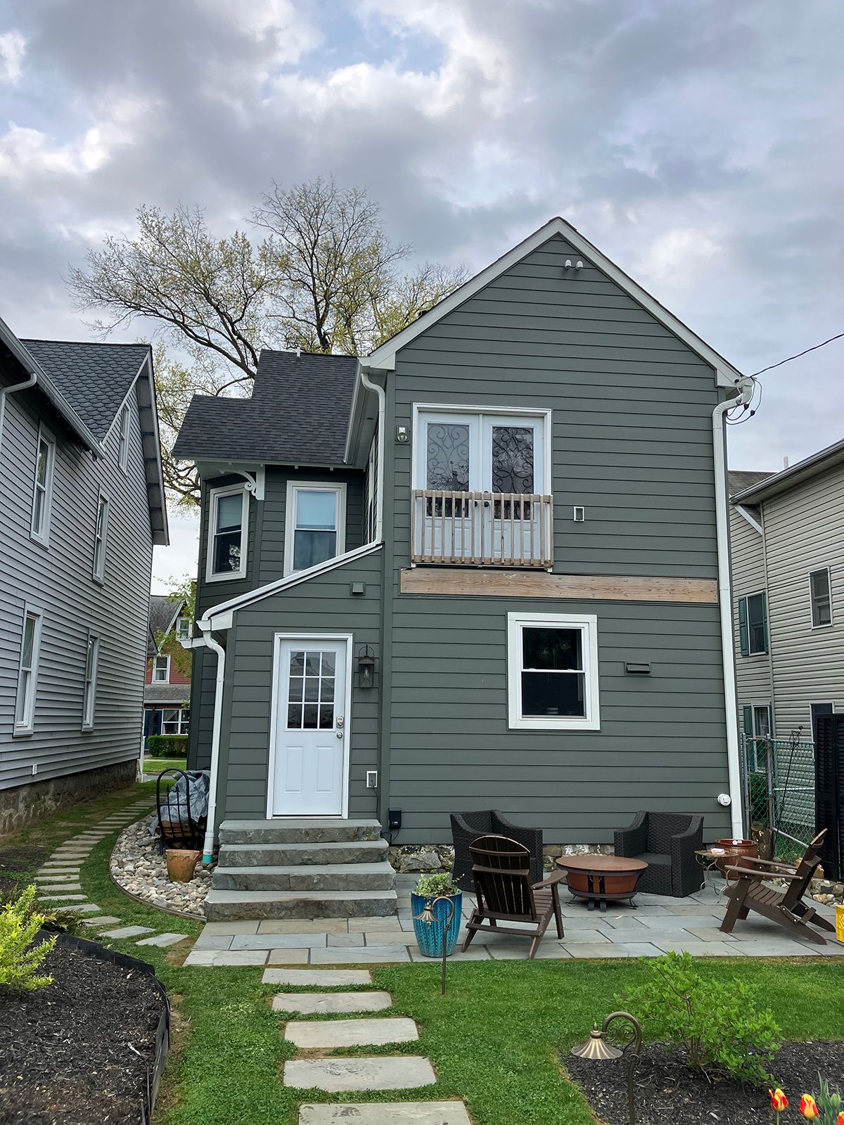 A gray house with a white door and a patio in front of it.