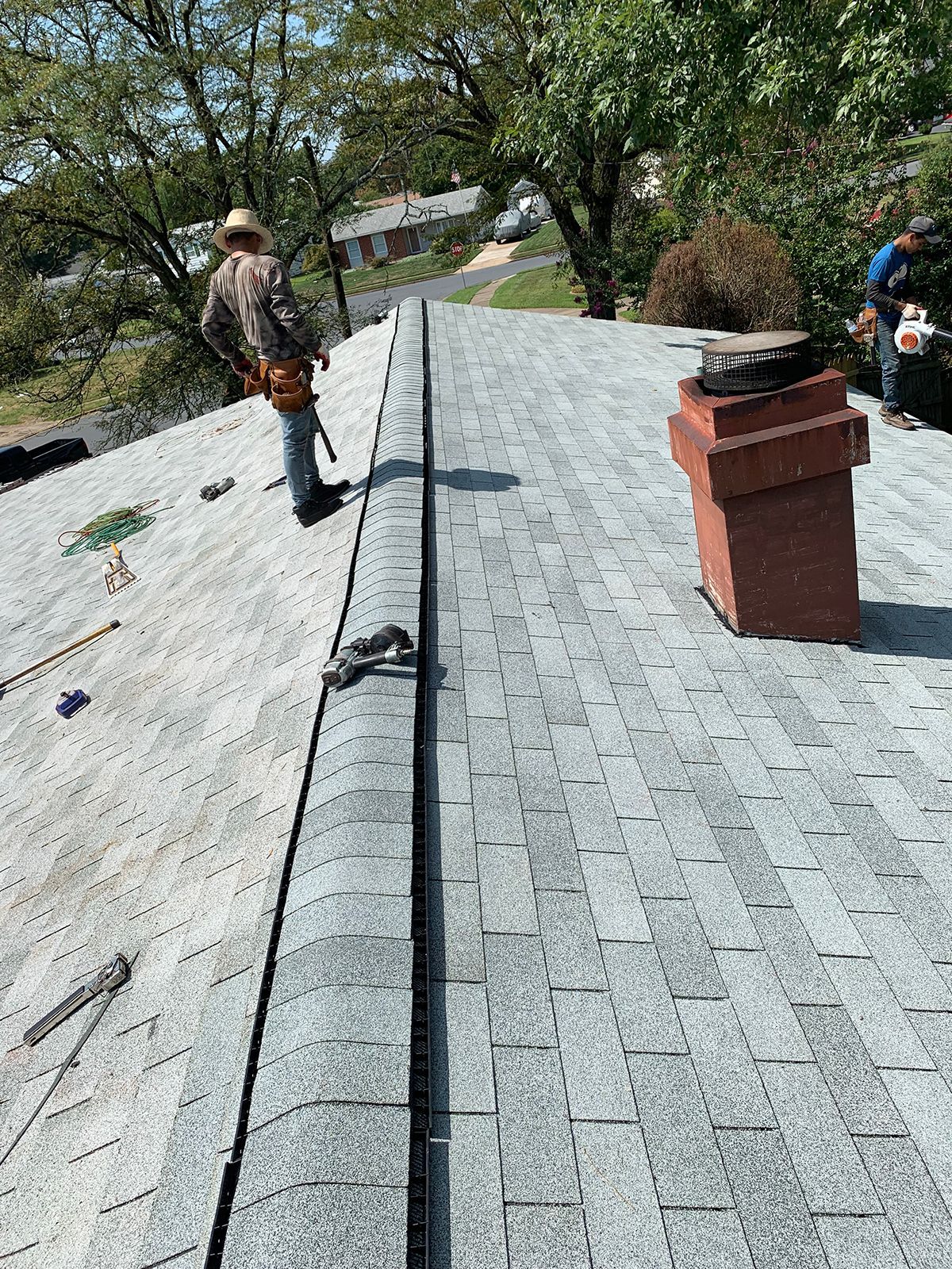 A man is standing on top of a roof next to a chimney.