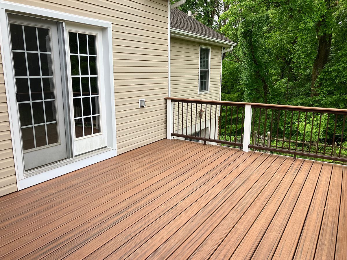 A wooden deck with a railing and sliding glass doors on the side of a house.