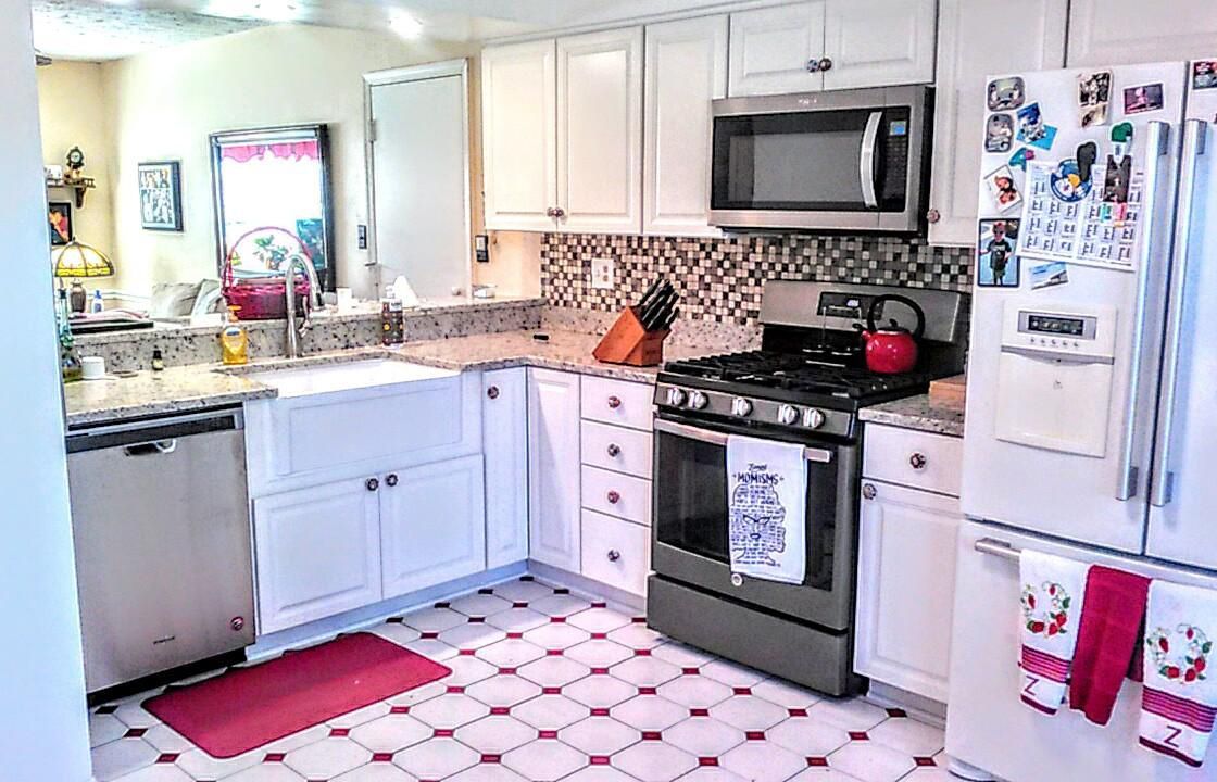 A kitchen with white cabinets , a stove , a refrigerator , a microwave , and a sink.