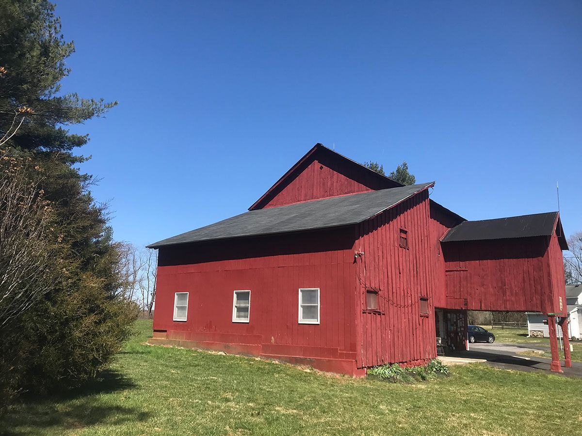 A red barn with a black roof is sitting in the middle of a grassy field.