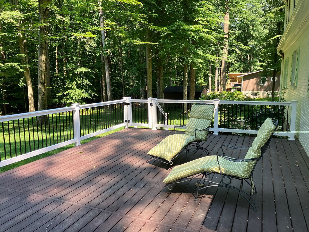 A wooden deck with chairs and a white railing surrounded by trees.