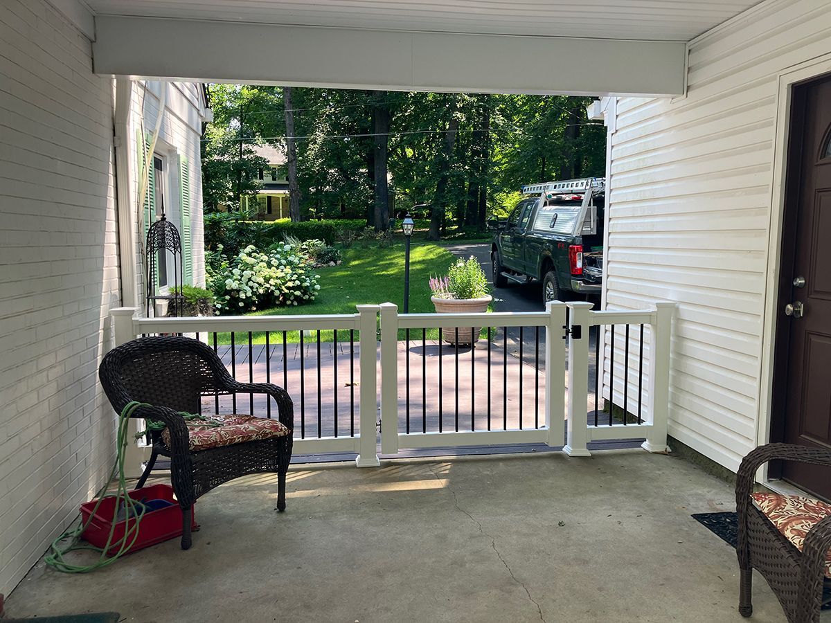 A porch with a chair and a fence with a car parked in the background.