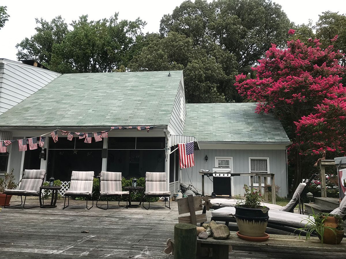 A white house with a green roof and a patio with chairs and a grill.