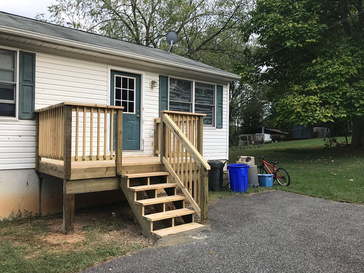 A small white house with a wooden deck and stairs.