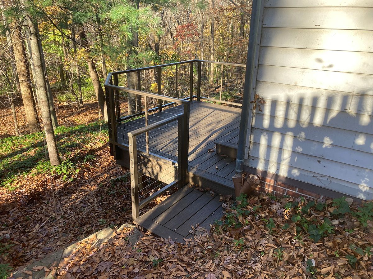 A wooden deck with stairs leading up to a house in the woods.