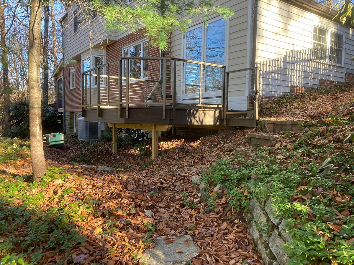 A house with a deck in front of it surrounded by trees and leaves.